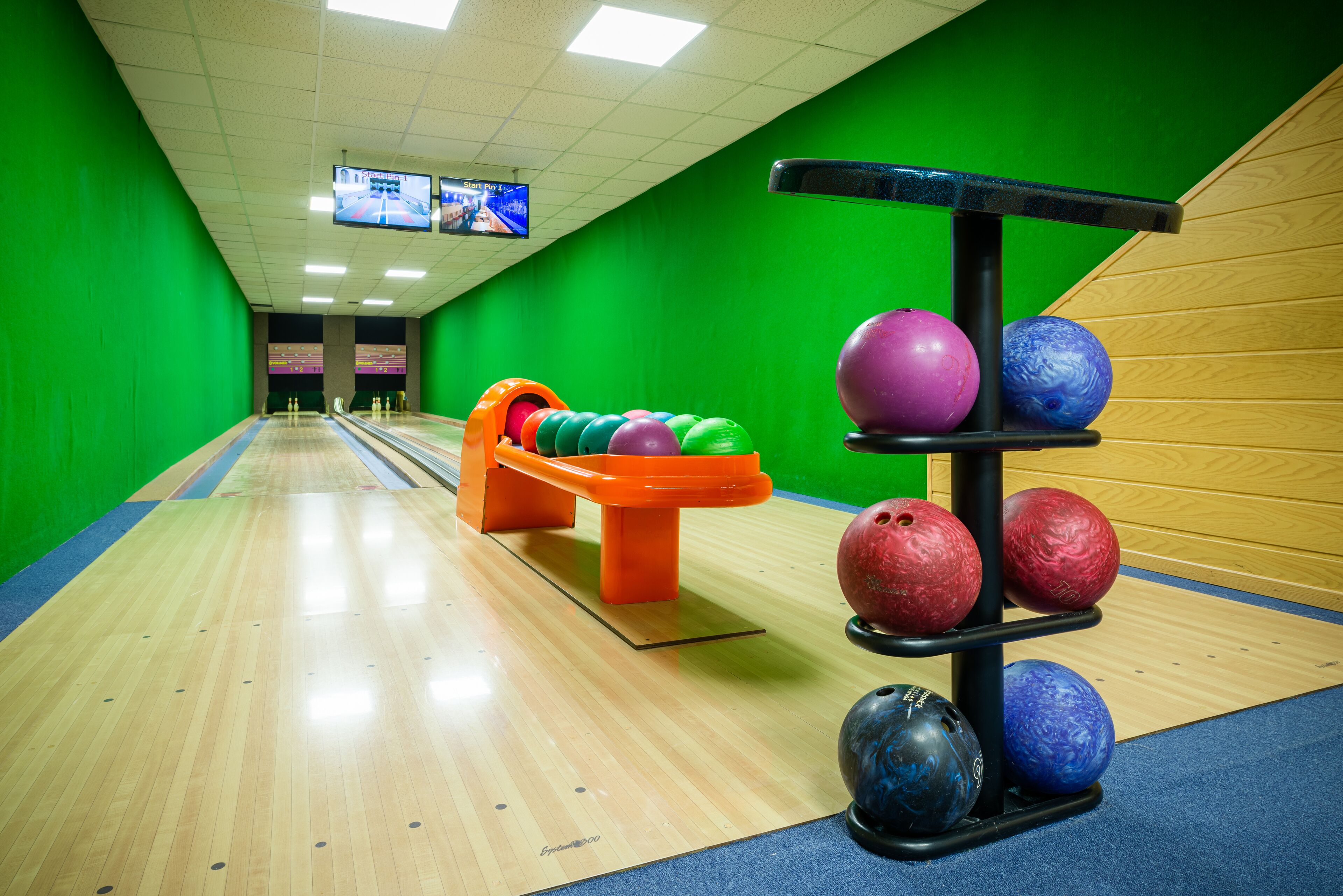 A bowling alley with a wooden floor, green walls, and a bowling ball rack.