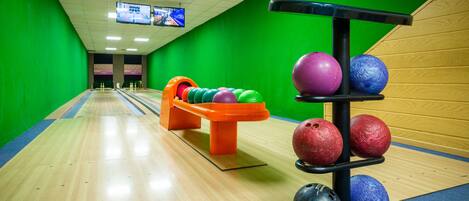 A bowling alley with a wooden floor, green walls, and a bowling ball rack.