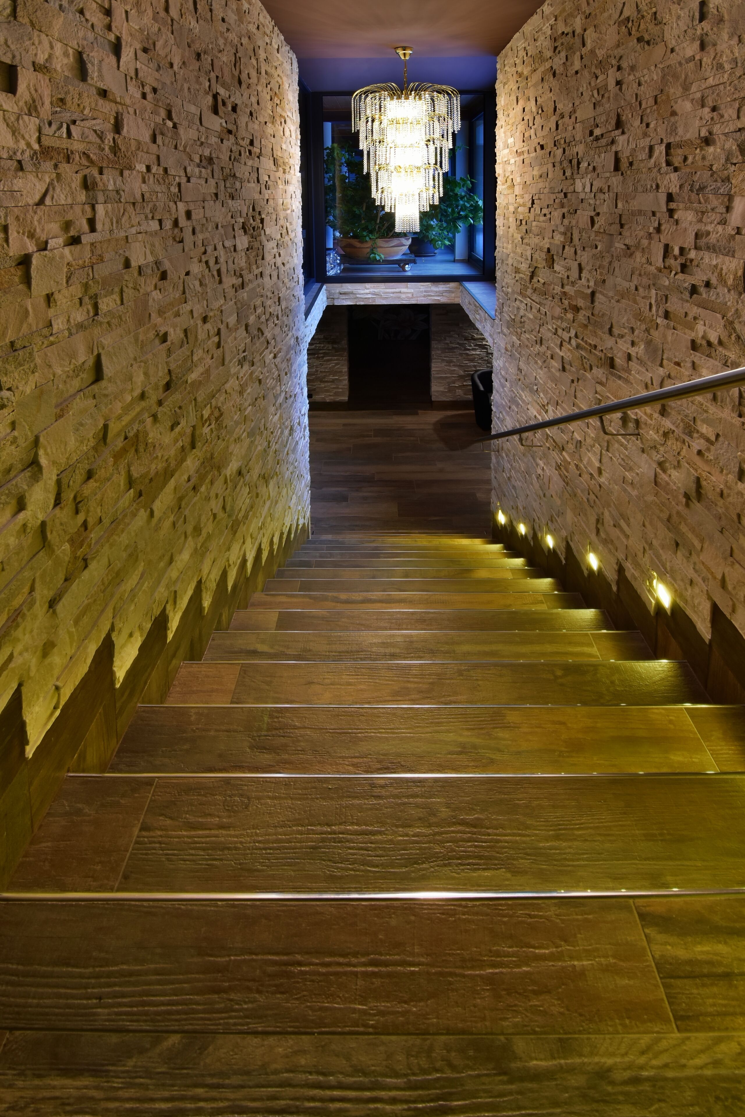 Una escalera flanqueada por paredes de piedra, que conduce a una habitación con candelabro y plantas en macetas.