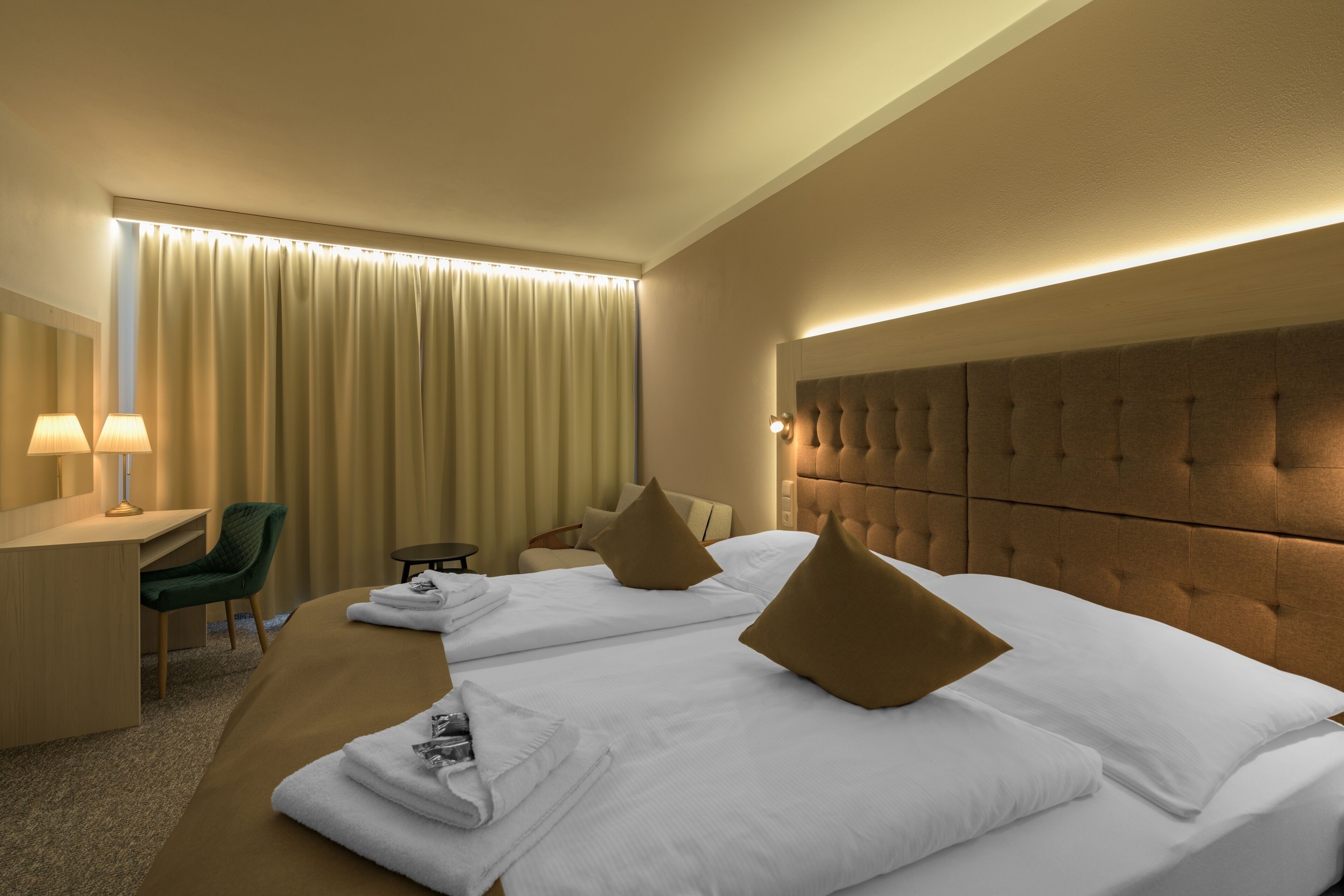 Habitación de hotel con dos camas, un escritorio, una silla y un ventanal con cortinas.