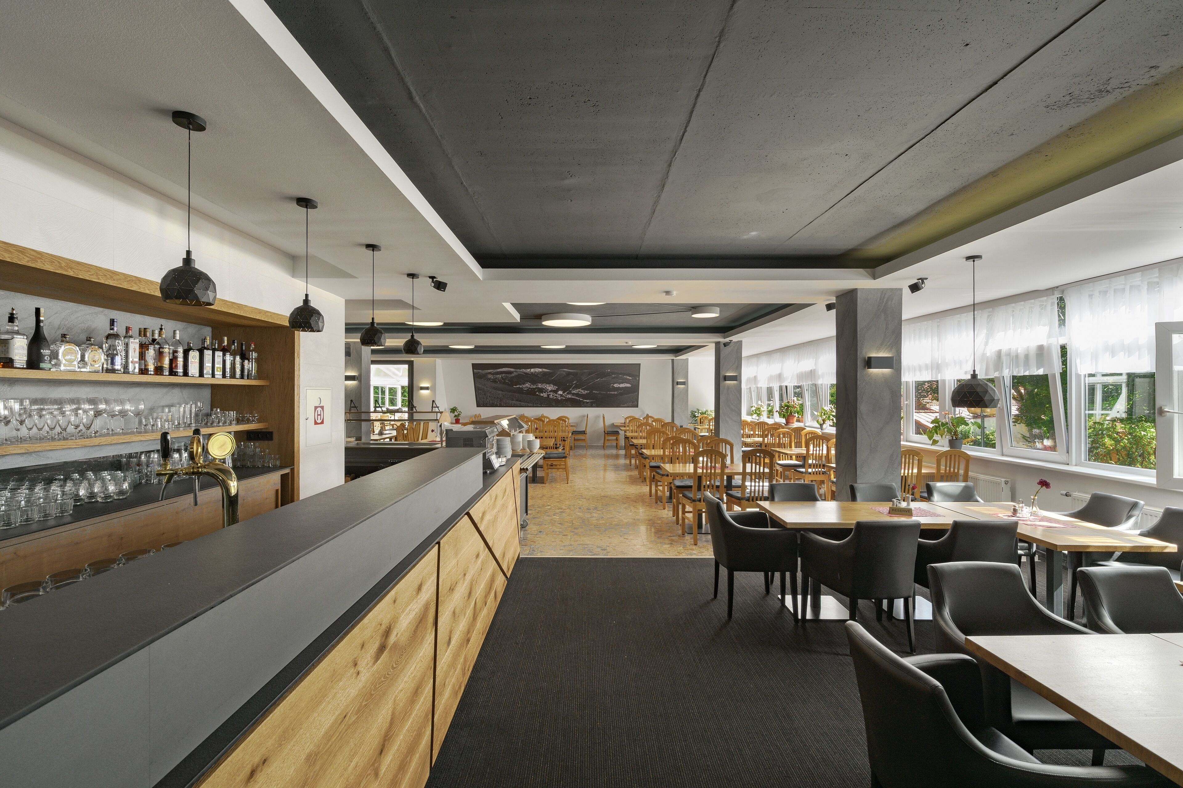 A modern bar area with a counter, shelves of bottles, and glasses. There are wooden tables and chairs arranged for dining.