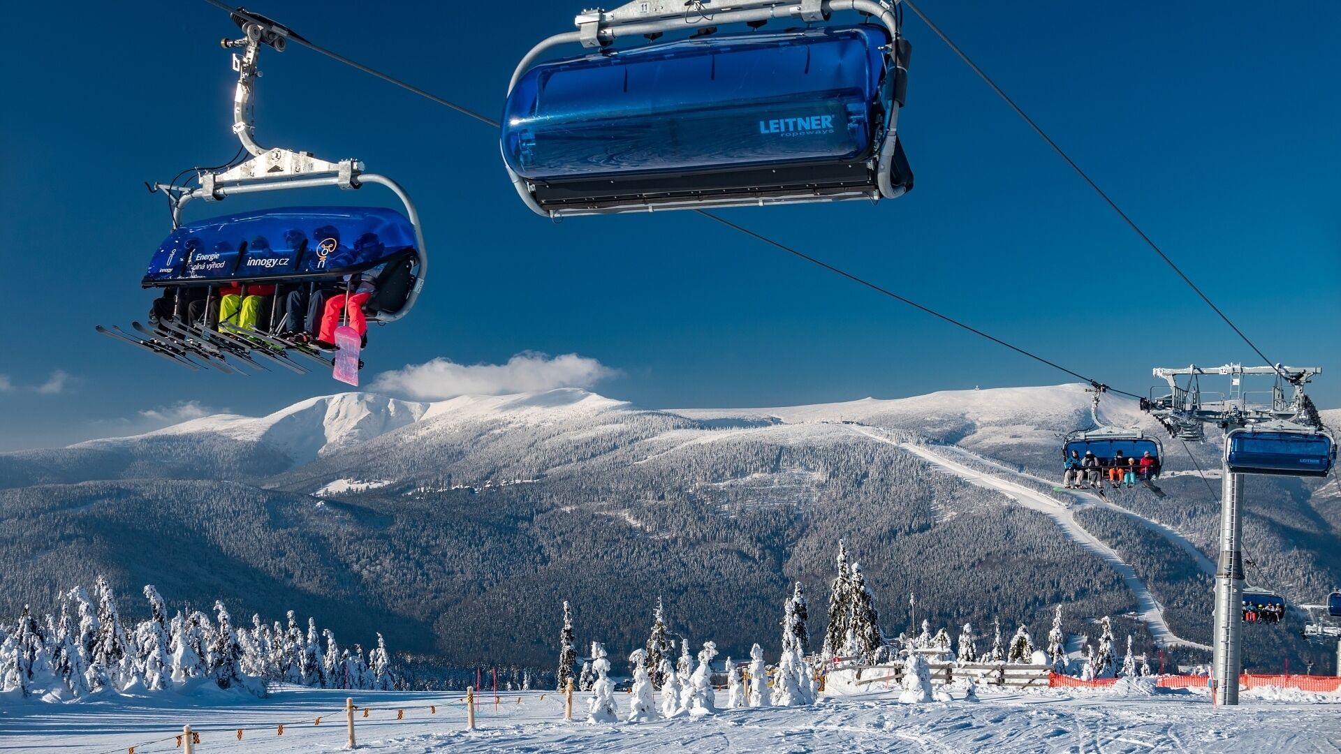 A ski lift with a clear view of snow-covered mountains and trees in the background.