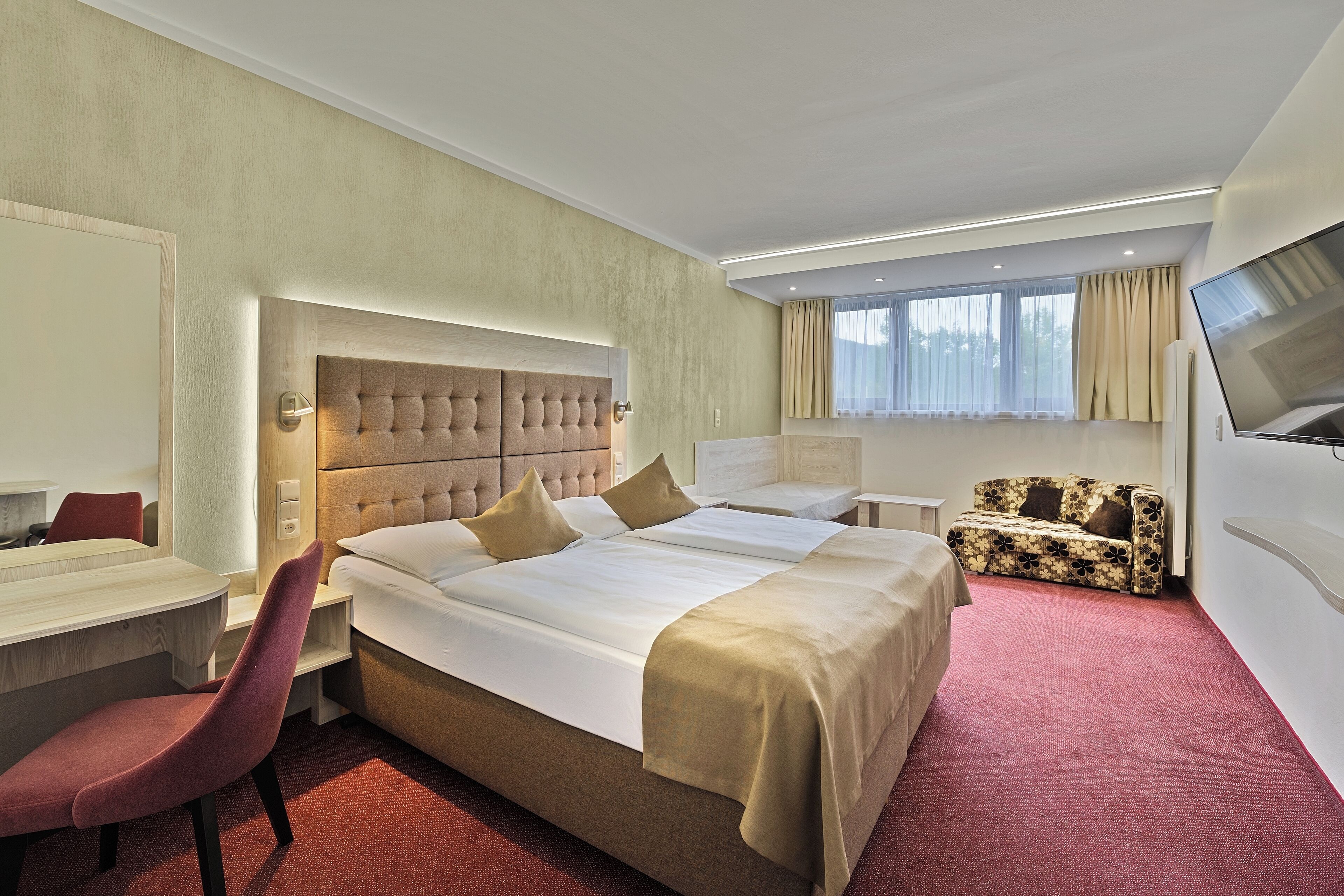 A hotel room with a large bed, a desk, a chair, a sofa, and a TV.