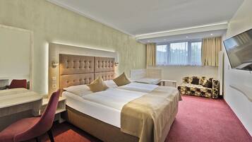 A hotel room with a large bed, a desk, a chair, a sofa, and a TV.