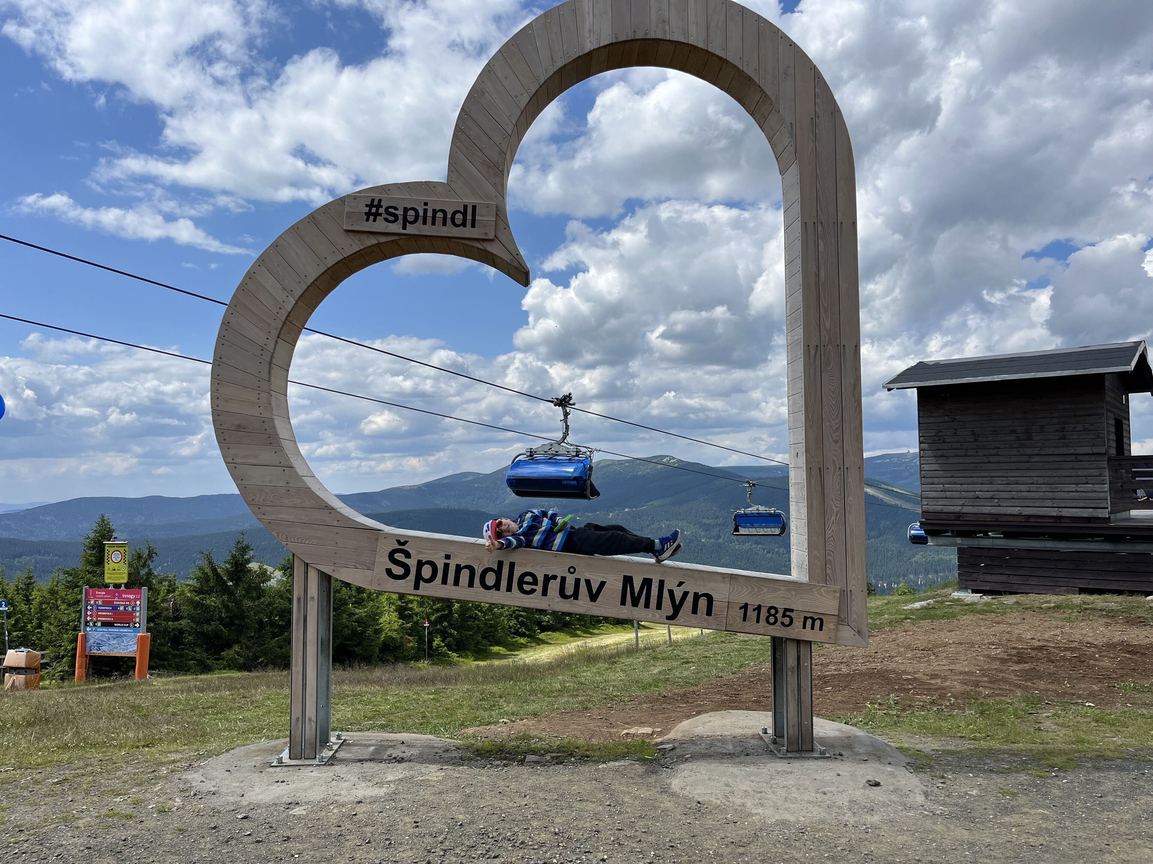 A wooden sign with a ski lift and mountains in the background.