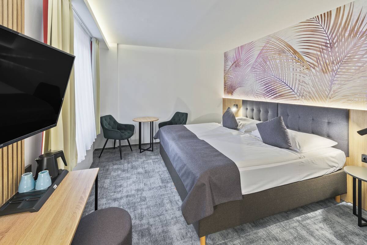 A hotel room with a large bed, a flat-screen TV, a small table, two chairs, and a decorative wall piece.