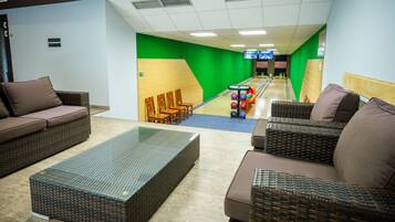 A bowling alley with green walls, wooden seating, and a glass coffee table.