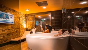 A modern spa area with multiple hot tubs and a television screen displaying a news program. - Wellness Hotel Astra (Spindleruv Mlyn)