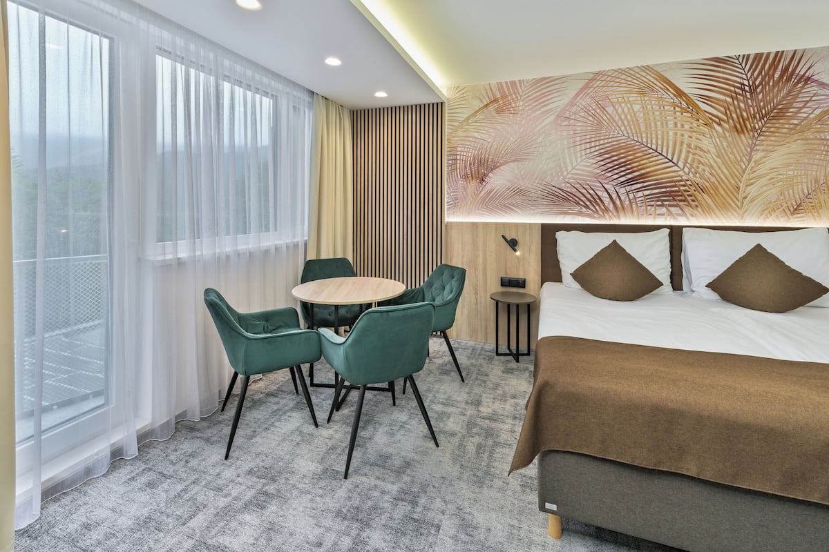 A hotel room with a bed, a round table with chairs, a view of the outdoors through sheer curtains, and a large wall mural.