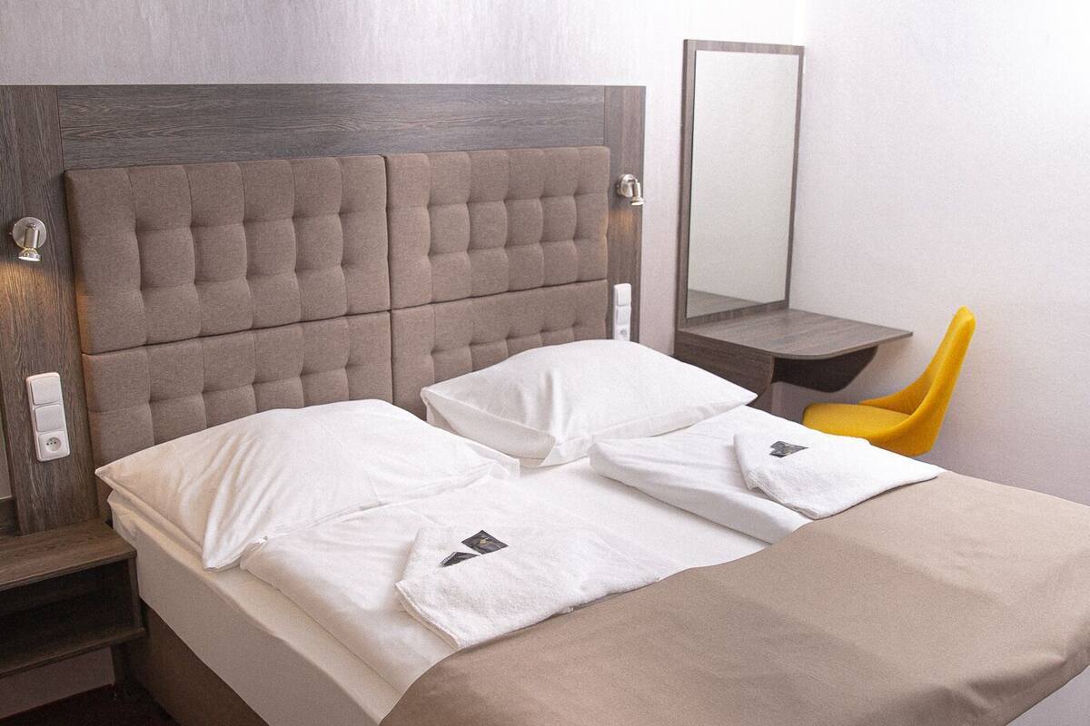 A hotel room with a large bed, a wooden headboard, a bedside table, a chair, and a mirror.