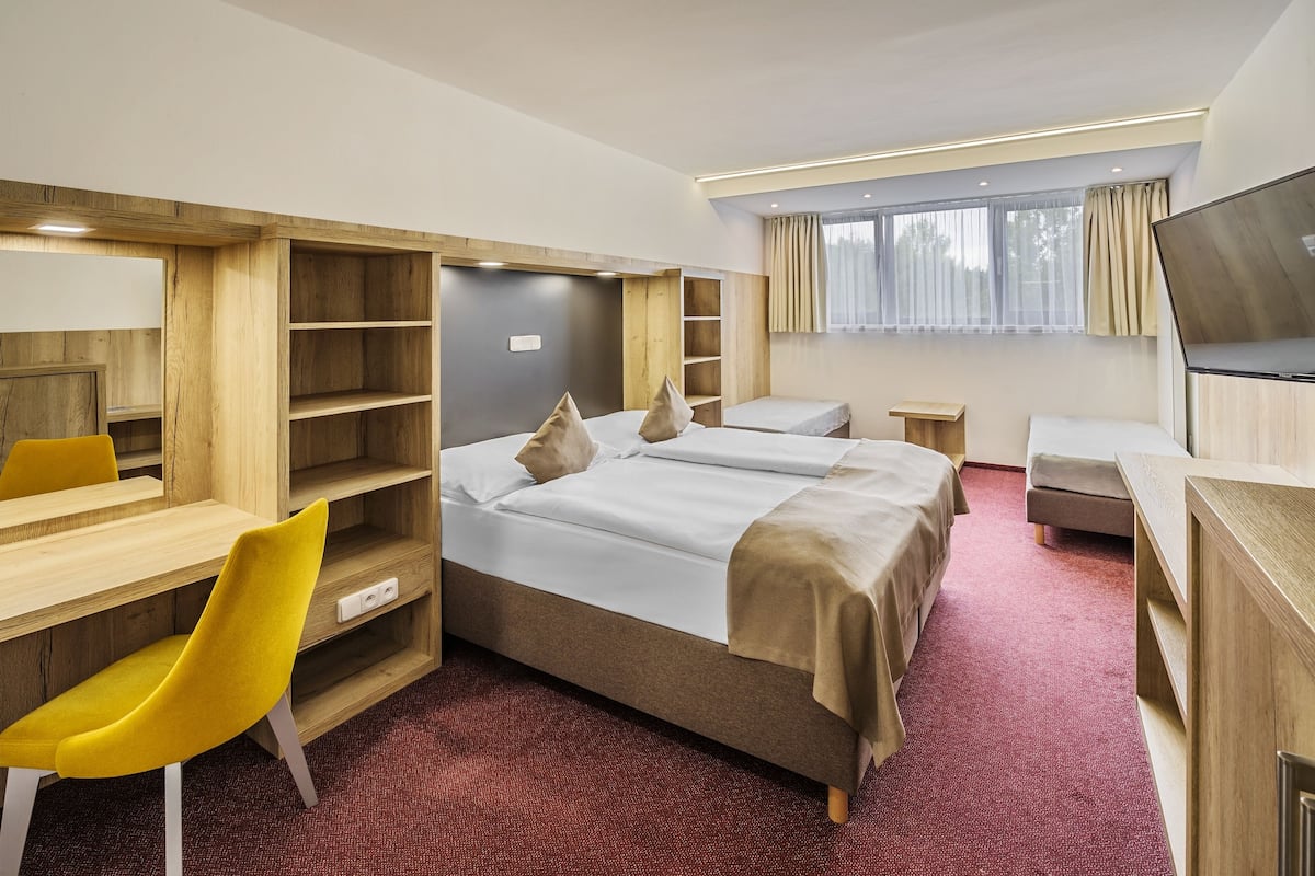 A hotel room with a bed, two bedside tables, a desk with a chair, a TV, and built-in shelving.