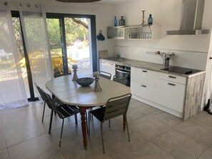 Uma cozinha moderna com uma mesa de jantar, cadeiras e vista para o exterior por uma porta de vidro.