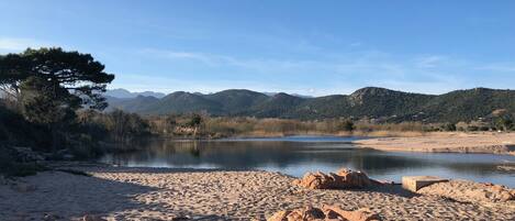 A beach with sand and rocks, a body of water, and mountains in the background.