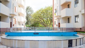 A swimming pool surrounded by a tiled walkway, with a building in the background. - Spacious one bedroom apartment in Kileleshwa Nairobi (Nairobi)