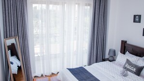 A bedroom with a bed, a mirror, a window with curtains, a bedside lamp, and a wall with a motivational quote. - Spacious one bedroom apartment in Kileleshwa Nairobi (Nairobi)
