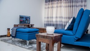 A modern living room with a blue sofa, a wooden coffee table, and a television on a stand. - Spacious one bedroom apartment in Kileleshwa Nairobi (Nairobi)