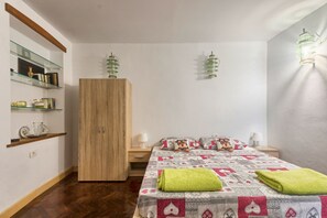 Quarto com guarda-roupa de madeira, cama com colcha estampada e duas luminárias fixadas na parede.