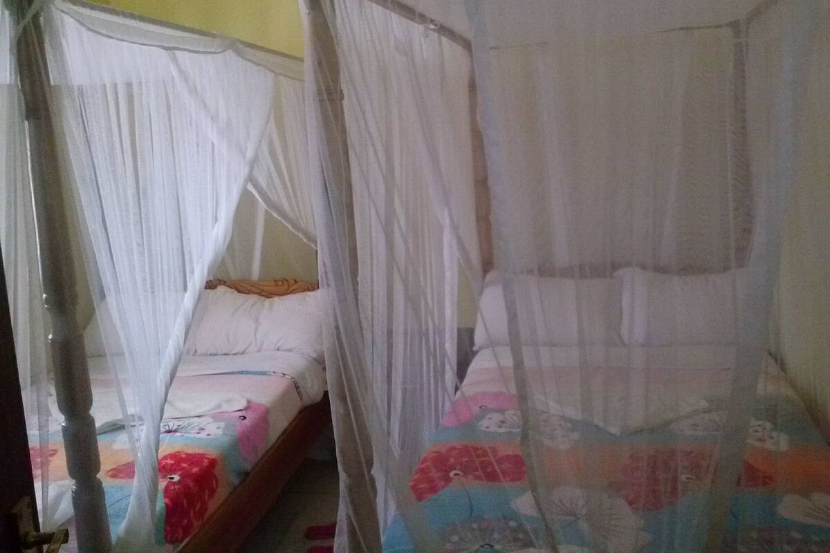 Dos camas individuales con mosquiteros, estructura de madera y colcha colorida.