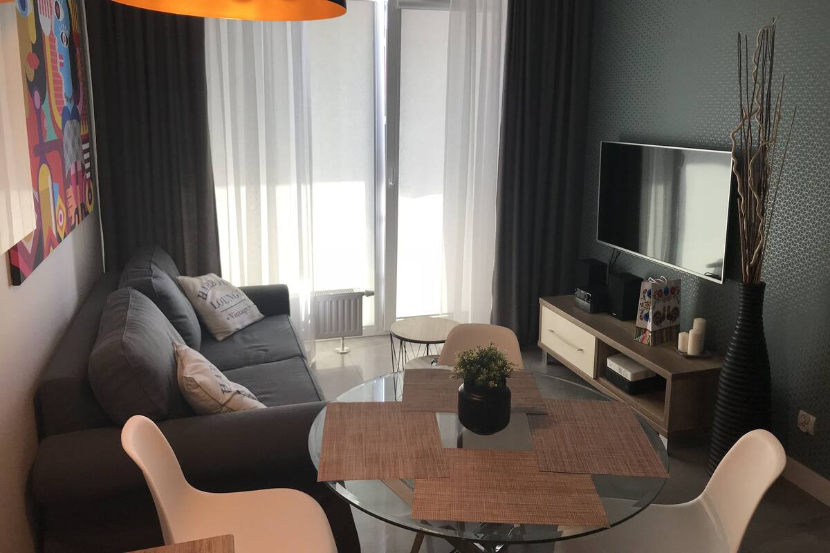 Uma sala de estar moderna com um sofá, uma mesa de centro de vidro e uma televisão.