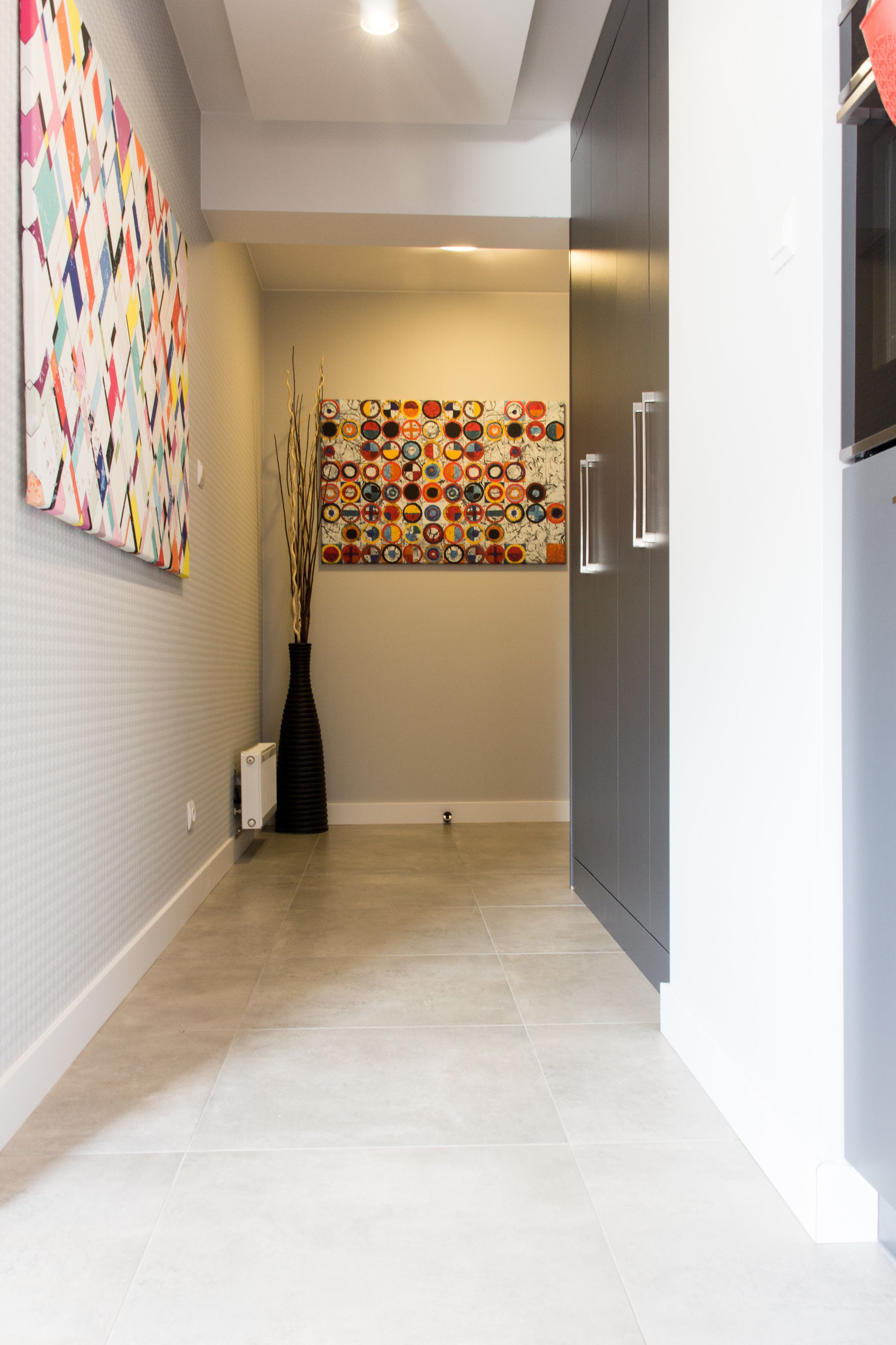 A modern kitchen with a tiled floor, a refrigerator, and a wall with colorful circular patterns.