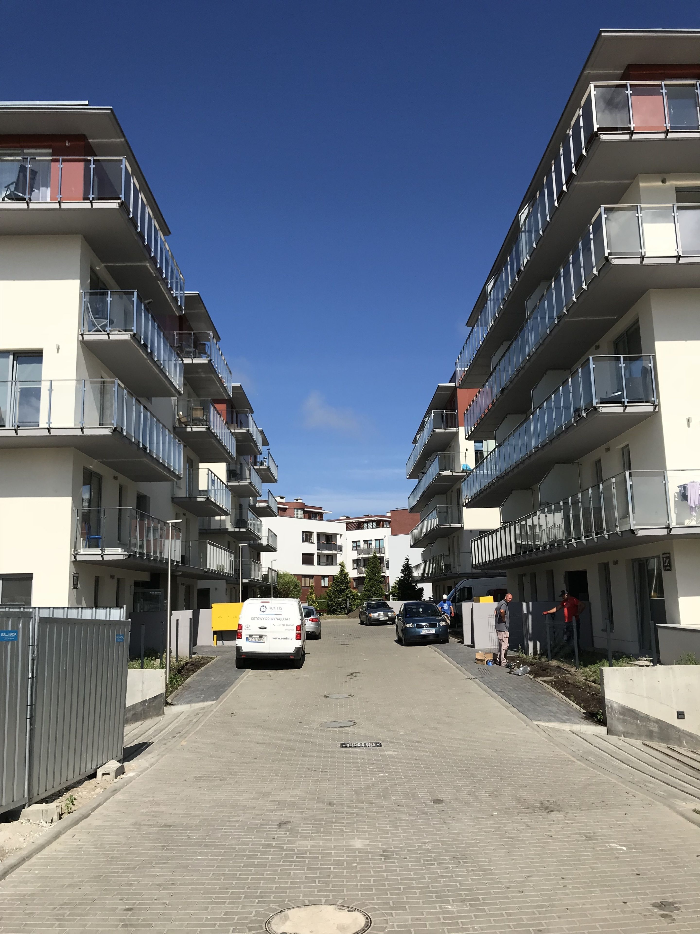 A multi-story residential building with balconies, a paved street, and parked cars.