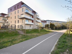 A multi-story residential building with balconies, a paved pathway, and a grassy area.