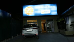 A white car parked in front of a building with a large illuminated sign that reads "Hotel Aangan Regency" and "goibibo". - Hotel Aangan Regency (Shimla)