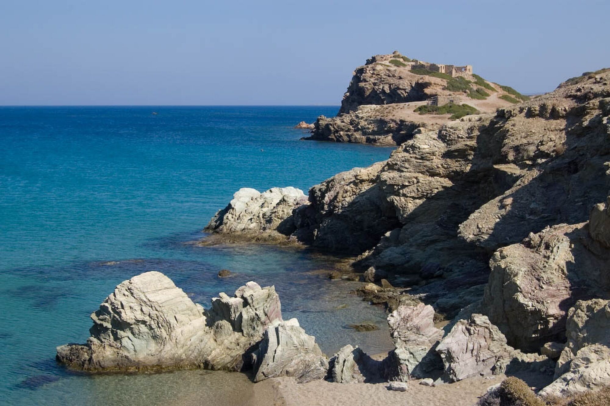 A rocky coastline with clear blue water and a historical building on a hill.