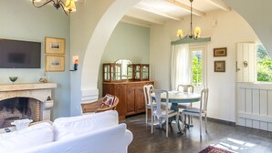 A cozy living room with a fireplace, white furniture, and a dining area with a table and chairs. - Charming Cretan House, Jasmine (Σητεία)