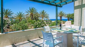 A terrace with white chairs and a table set for dining, overlooking a view of palm trees and the ocean. - Charming Cretan House, Jasmine (Σητεία)