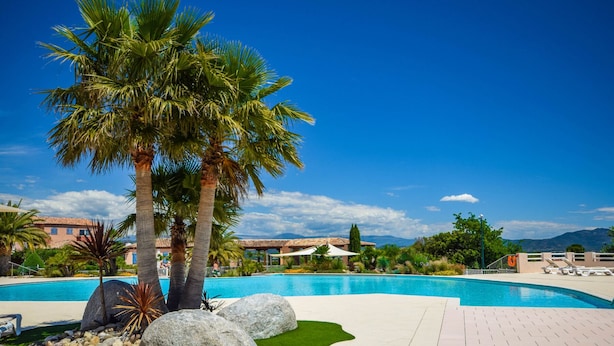 Area piscina con palme, cielo azzurro limpido e montagne sullo sfondo.