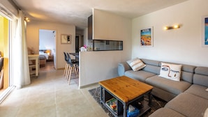Un soggiorno moderno con un divano grigio, un tavolino in legno e una zona cucina visibile attraverso un'apertura.