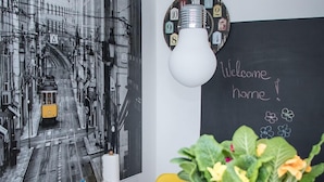 Una pintura en blanco y negro de un paisaje urbano, una pizarra con la leyenda 'Welcome home!' y una bombilla en la pared.