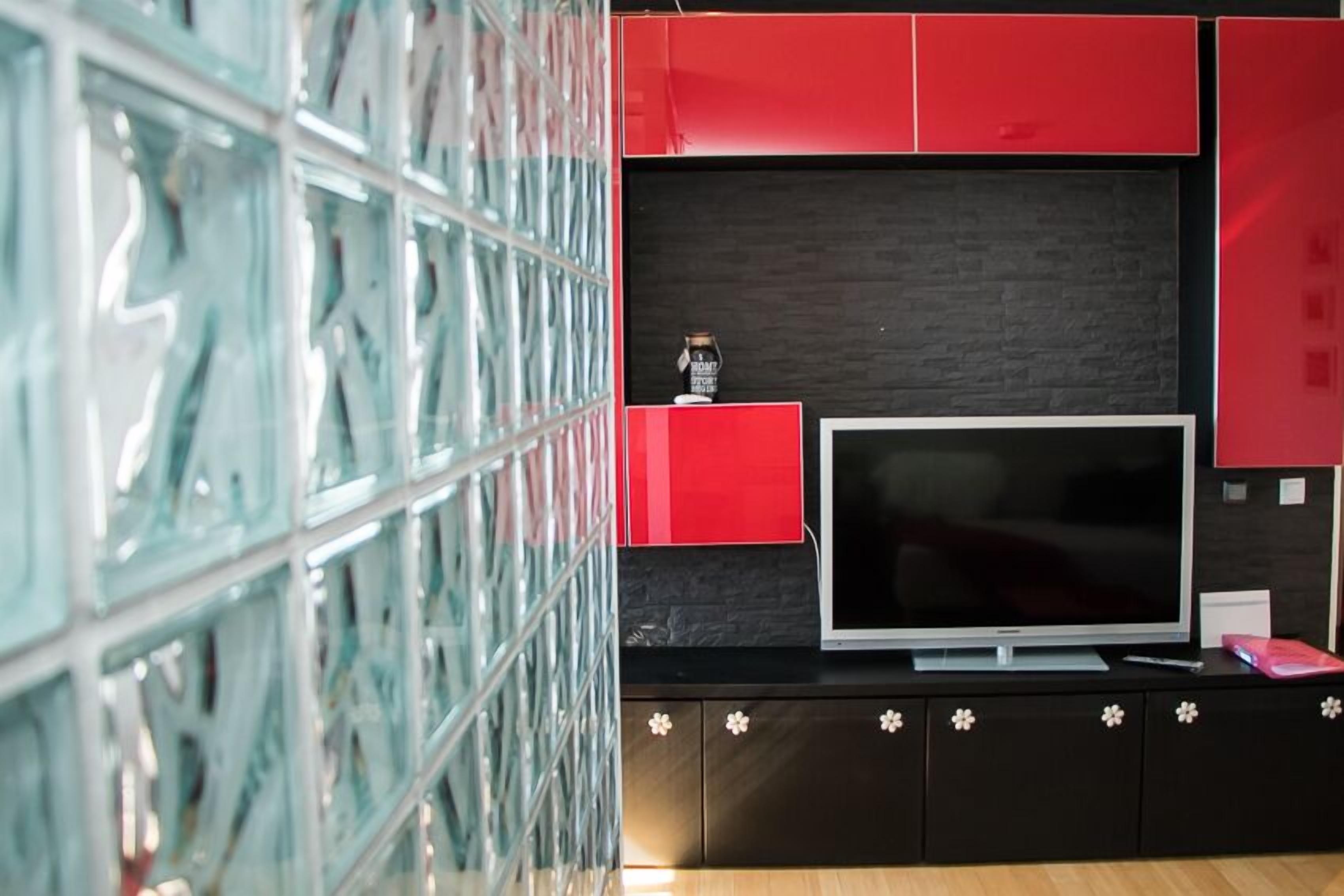 A modern living room with a large flat-screen TV, red and black cabinetry, and a glass wall.
