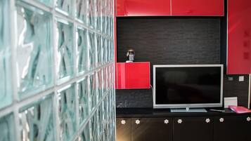 A modern living room with a large flat-screen TV, red and black cabinetry, and a glass wall.