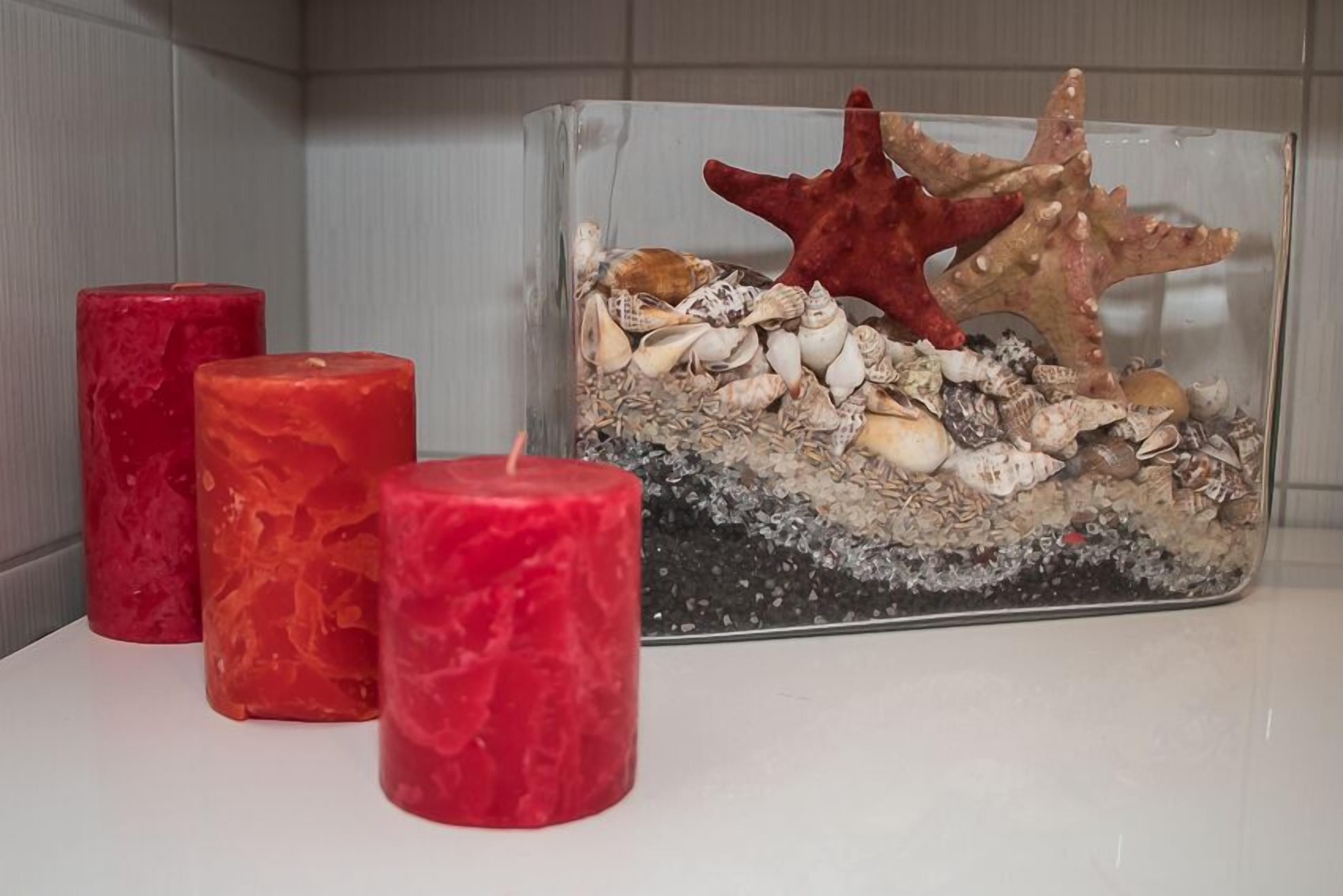 A glass container with seashells and a starfish, accompanied by three red candles on a white surface.