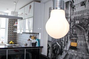A modern kitchen with a large light fixture, a tiled backsplash, and a cityscape mural on the wall. - Apartment Travel hub (Varazdin)