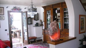 A cozy living room with a blue sofa, a patterned rug, a glass-top coffee table, and a cabinet with glass doors. - Green Rose bed and breakfast (Cesiomaggiore)