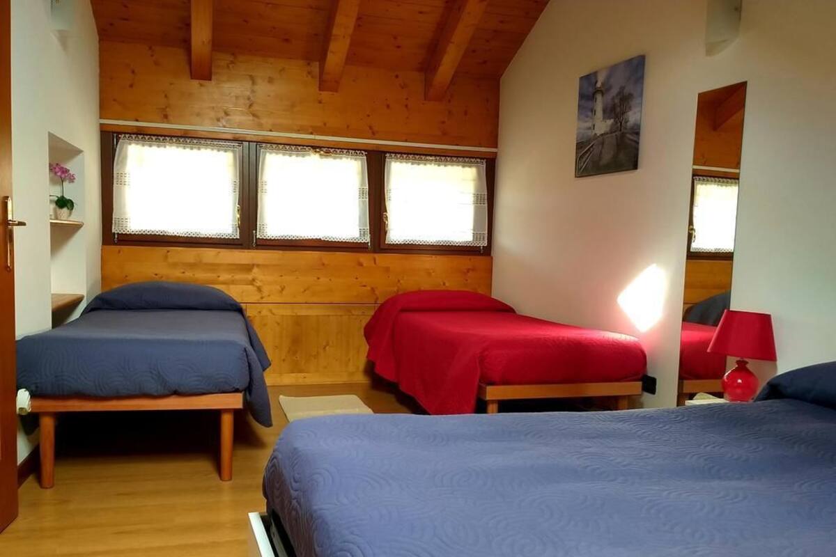 A room with three beds, wooden walls, and large windows with lace curtains.