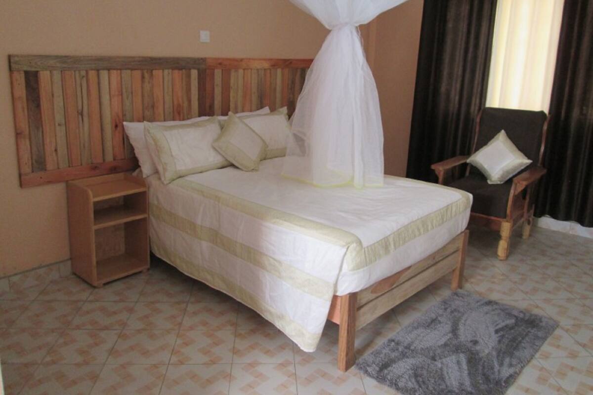 A bed with a wooden headboard, a bedside table, a chair, and a grey rug.
