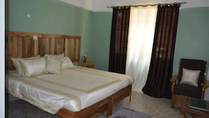 A bedroom with a wooden bed, a nightstand, a chair, and a laptop on a small table. - Snow Peak Hotel (Chogoria)
