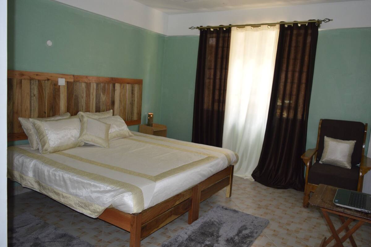 A bedroom with a wooden bed, a nightstand, a chair, and a laptop on a small table.