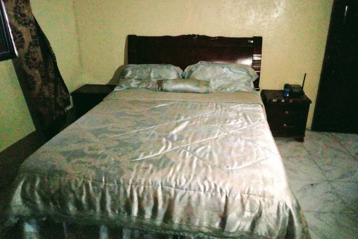A bed with a patterned bedspread, a wooden headboard, and a bedside table with a lamp.