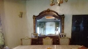 Comedor con una mesa rectangular, cuatro sillas, un espejo grande y una puerta oscura.