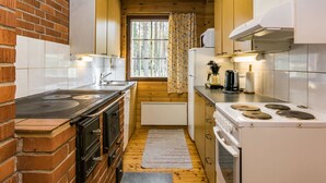A compact kitchen with a brick wall, wooden cabinets, a stove, and a window with curtains. - Mäntyniemi by Interhome (Mäntyharju)