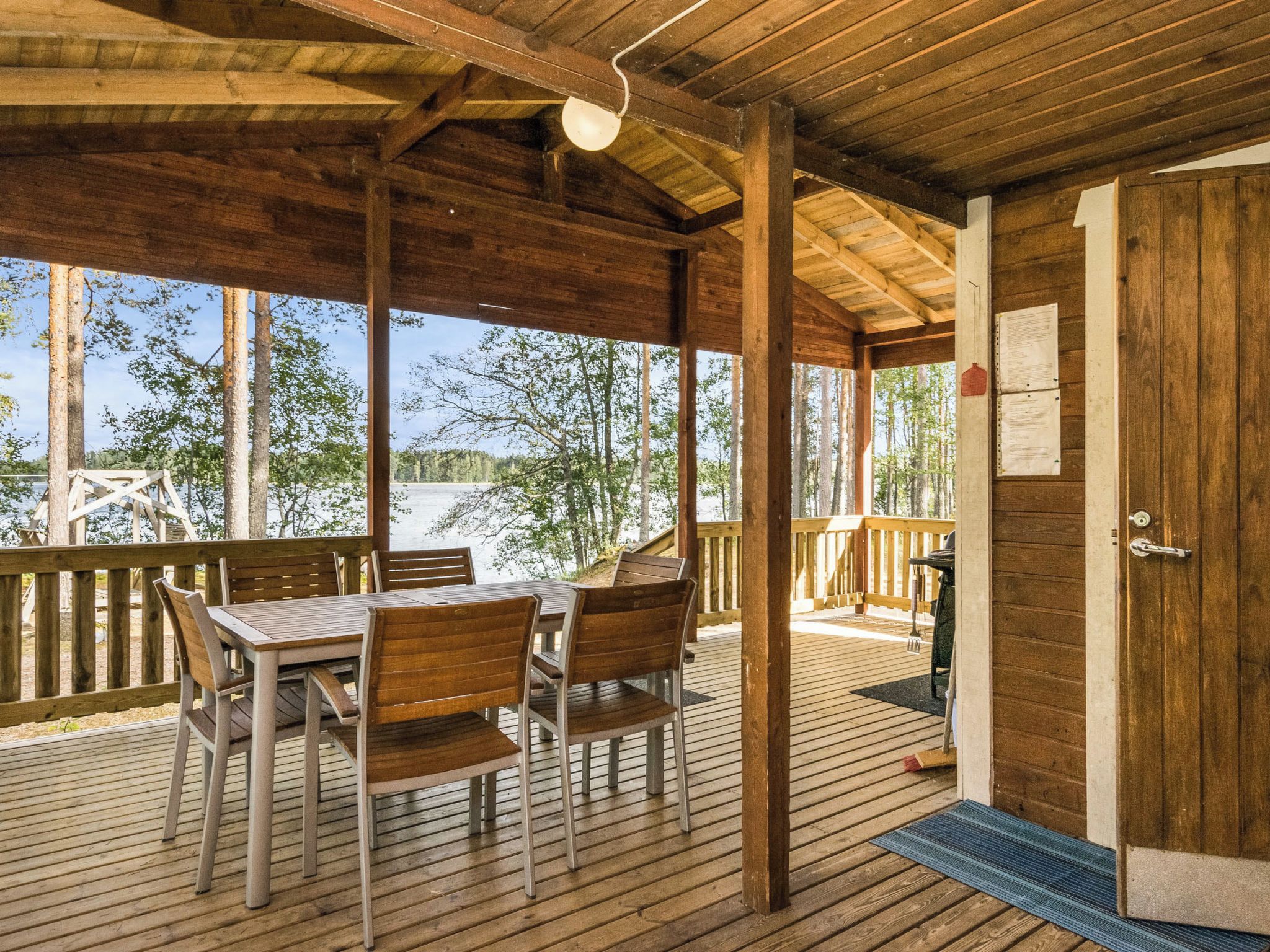 A covered outdoor area with a wooden table and chairs, a grill, and a view of trees and water.