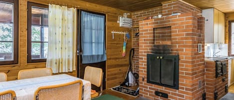 A wooden cabin interior with a brick fireplace, dining table, chairs, and a kitchen area.