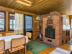 Interior de una cabaña de madera con chimenea de ladrillo, mesa de comedor, sillas y una zona de cocina.