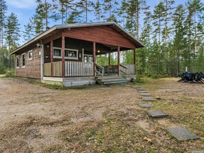 Une cabane dotée d’une véranda, d’un escalier menant à l’entrée et surplombant un paysage boisé.