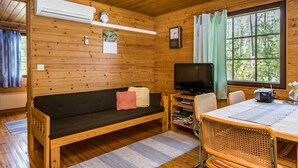 A cozy cabin interior with a wooden floor, a sofa with cushions, a television, a dining table with chairs, and a window with curtains. - Mäntyniemi by Interhome (Mäntyharju)